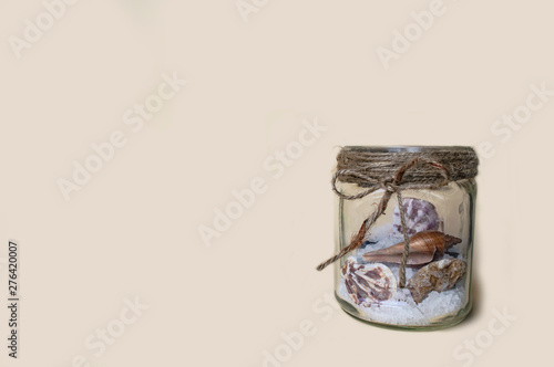 glass jar with sea salt and shells yellow background