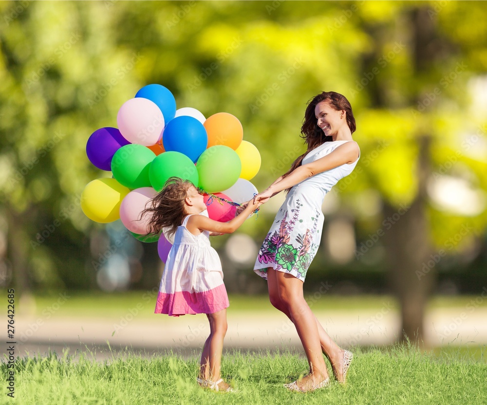 Beautiful happy mother with daughter having fun in green field holding colorful balloons - obrazy, fototapety, plakaty 