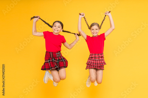 Feeling playful. beauty look. happy children on yellow wall. childhood happiness. trendy school uniform. funny jump. red fashion girls. english style fashion. happy little girls in checkered skirt