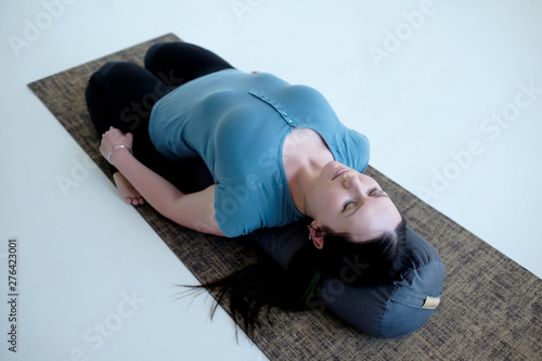 Cauacasian woman resting in reclining hero pose or Supta Virasana with bolster, stretching after practice. Studio shot
