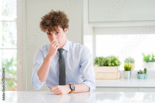 Young business man wearing a tie smelling something stinky and disgusting, intolerable smell, holding breath with fingers on nose. Bad smells concept. © Krakenimages.com