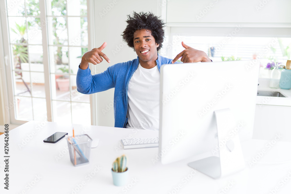 Fototapeta premium African American man working using computer looking confident with smile on face, pointing oneself with fingers proud and happy.