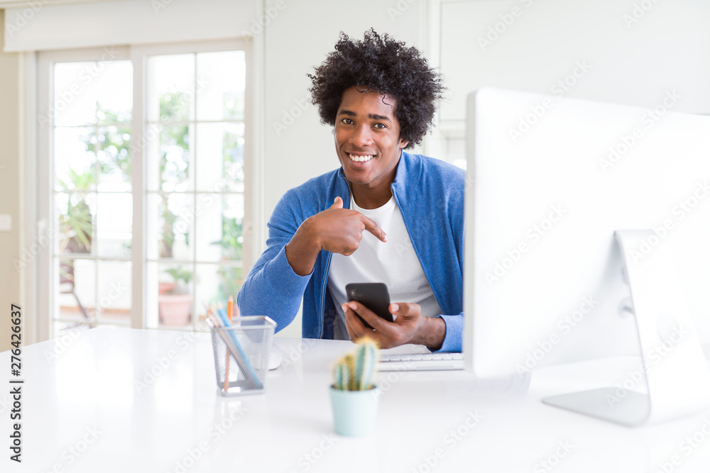 African American man working using smartphone and computer with surprise face pointing finger to himself