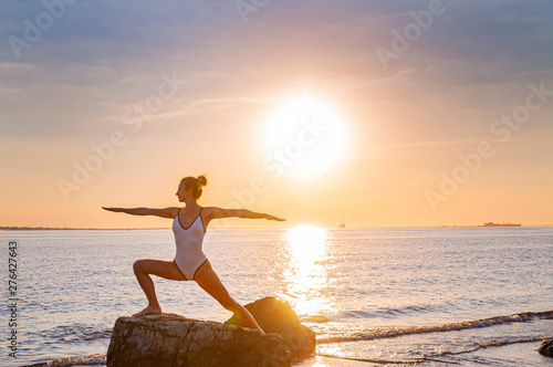 Woman is practicing yoga at sunset on stone. Silhouette of yoga woman on the beach at sunset.