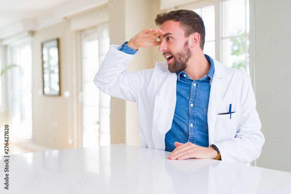Handsome doctor man wearing medical coat at the clinic very happy and smiling looking far away with hand over head. Searching concept. Handsome doctor man wearing medical coat at the clinic very happy and smiling looking far away with hand over head. Searching concept.