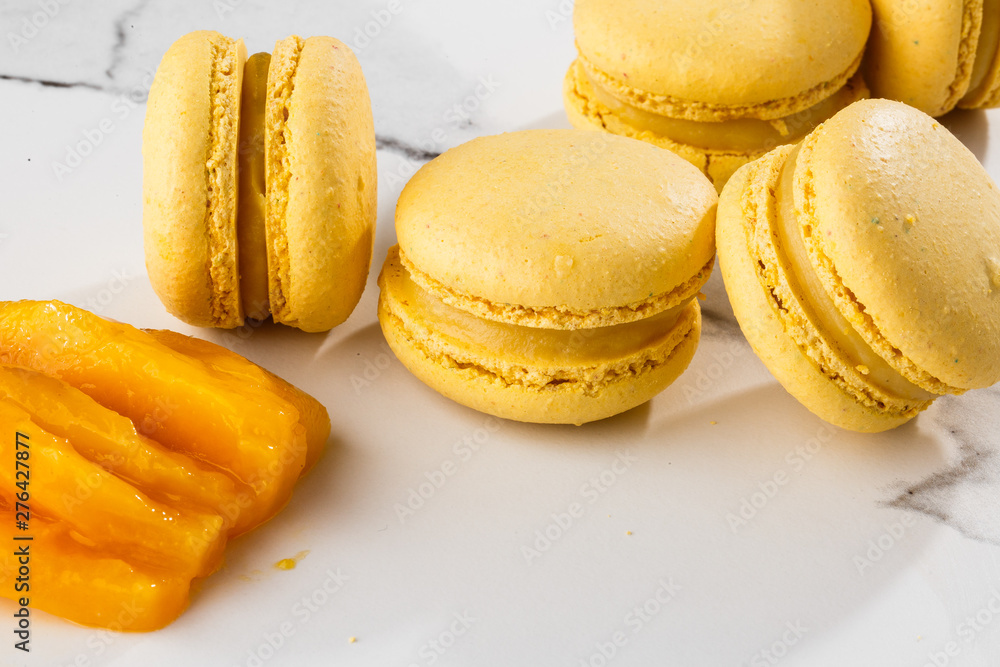 French macaroons isolated. Selective focus. Beautiful yellow macaroons with sliced mango on marble background. Stylish arrangement sweet. Flat lay, top view. Macro photo. With copy space. French macaroons isolated. Selective focus. Beautiful yellow macaroons with sliced mango on marble background. Stylish arrangement sweet. Flat lay, top view. Macro photo. With copy space.