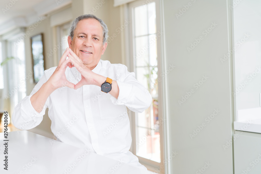 Handsome senior man at home smiling in love showing heart symbol and shape with hands. Romantic concept.