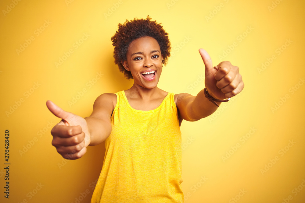 Beauitul african american woman wearing summer t-shirt over isolated yellow background approving doing positive gesture with hand, thumbs up smiling and happy for success. Winner gesture. Beauitul african american woman wearing summer t-shirt over isolated yellow background approving doing positive gesture with hand, thumbs up smiling and happy for success. Winner gesture.