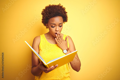 African american woman reading a book over yellow isolated background cover mouth with hand shocked with shame for mistake, expression of fear, scared in silence, secret concept