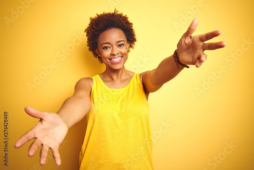 Fotografija Beauitul african american woman wearing summer t-shirt over isolated yellow background looking at the camera smiling with open arms for hug