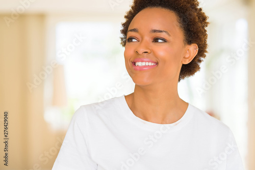 Young beautiful african american woman wearing casual white t-shirt looking away to side with smile on face, natural expression. Laughing confident.