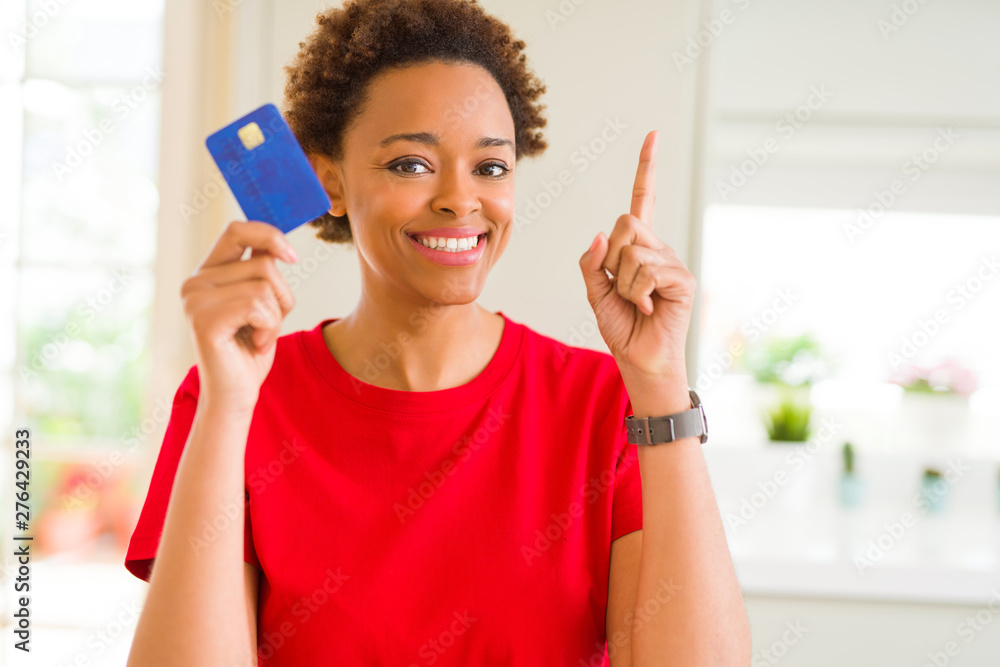 Young african american woman holding credit card surprised with an idea or question pointing finger with happy face, number one Young african american woman holding credit card surprised with an idea or question pointing finger with happy face, number one