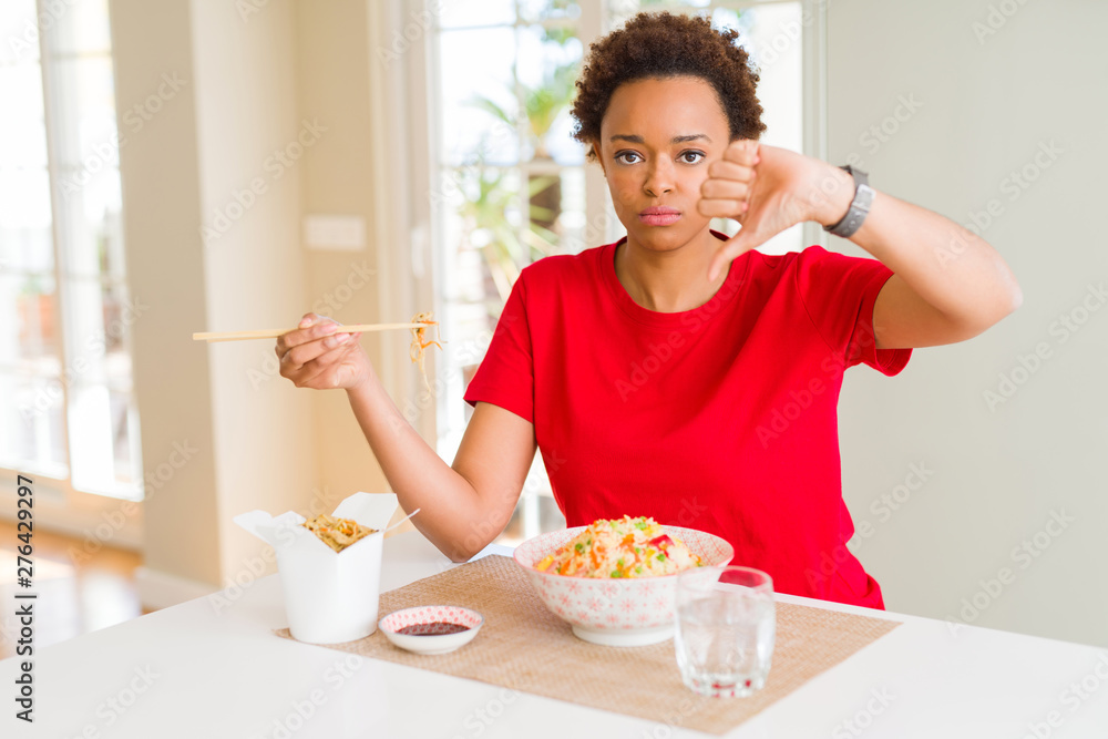 Young african american woman with afro hair eating asian food at home with angry face, negative sign showing dislike with thumbs down, rejection concept Young african american woman with afro hair eating asian food at home with angry face, negative sign showing dislike with thumbs down, rejection concept