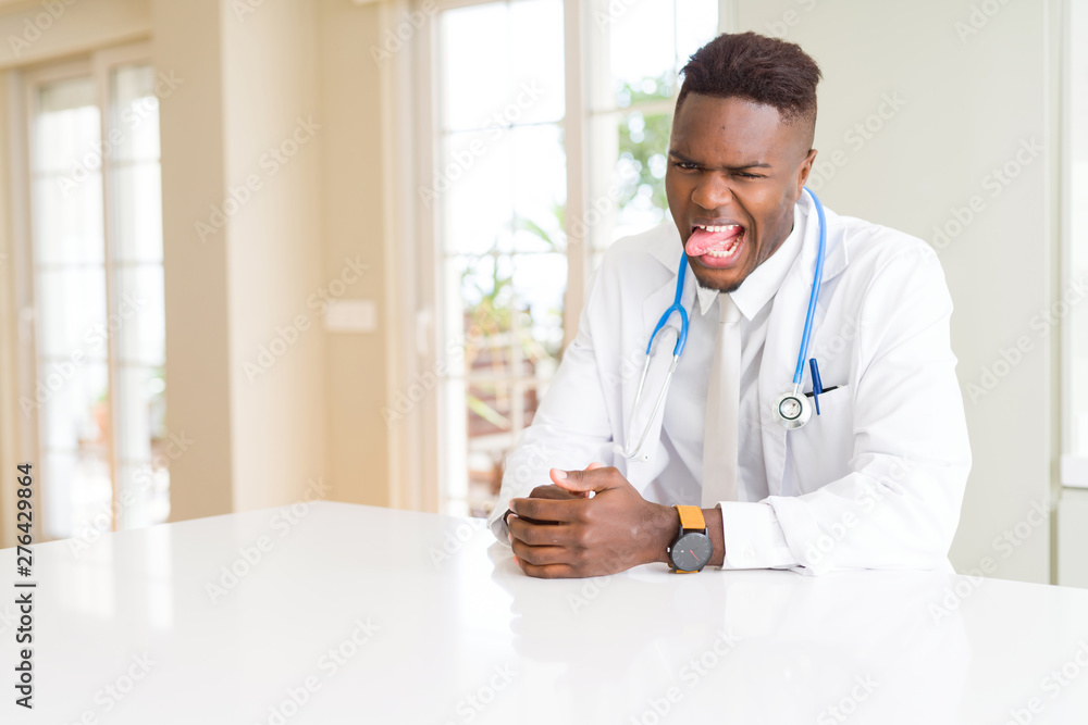 African american doctor man at the clinic sticking tongue out happy with funny expression. Emotion concept.