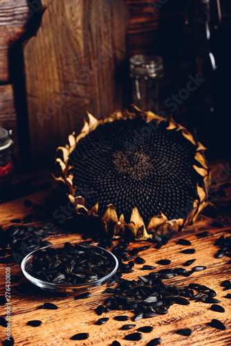 Roasted seeds on the glass saucer and dried sunflower over old wooden surface