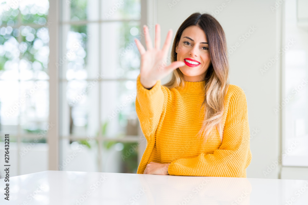 Young beautiful woman wearing winter sweater at home showing and pointing up with fingers number five while smiling confident and happy.