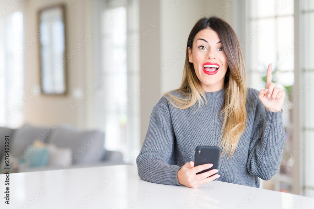 Young beautiful woman using smartphone at home surprised with an idea or question pointing finger with happy face, number one