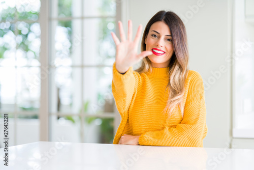 Young beautiful woman wearing winter sweater at home showing and pointing up with fingers number five while smiling confident and happy.