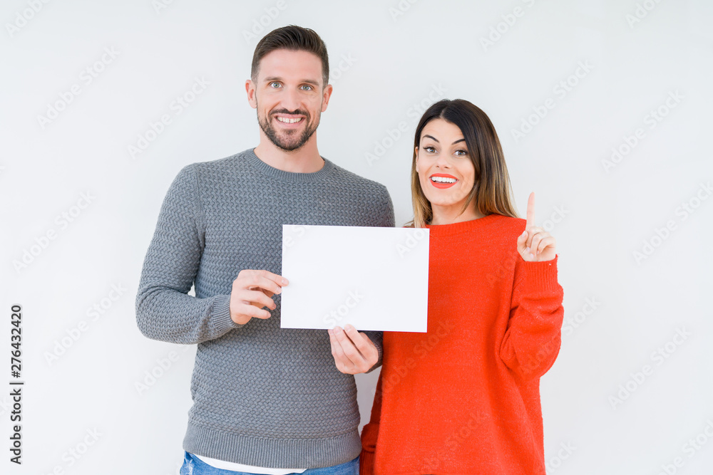 Young couple holding blank sheet paper over isolated background surprised with an idea or question pointing finger with happy face, number one Young couple holding blank sheet paper over isolated background surprised with an idea or question pointing finger with happy face, number one