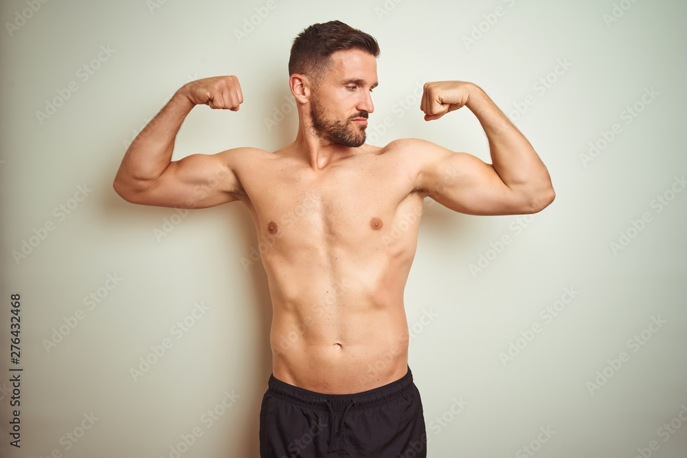 Young handsome shirtless man over isolated background showing arms muscles smiling proud. Fitness concept.