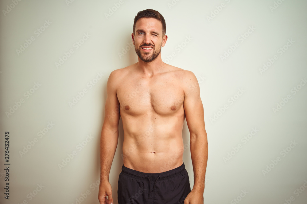Young handsome shirtless man over isolated background winking looking at the camera with sexy expression, cheerful and happy face.