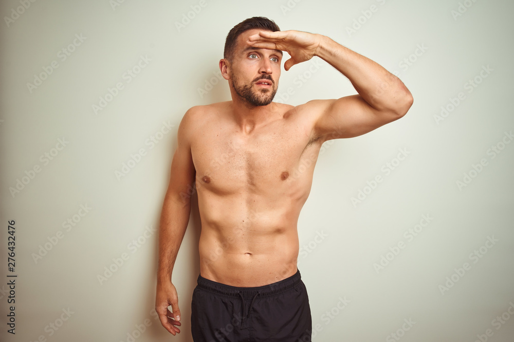 Young handsome shirtless man over isolated background very happy and smiling looking far away with hand over head. Searching concept.