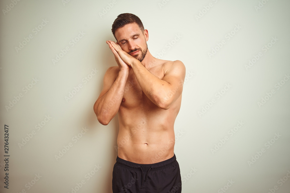 Fototapeta premium Young handsome shirtless man over isolated background sleeping tired dreaming and posing with hands together while smiling with closed eyes.