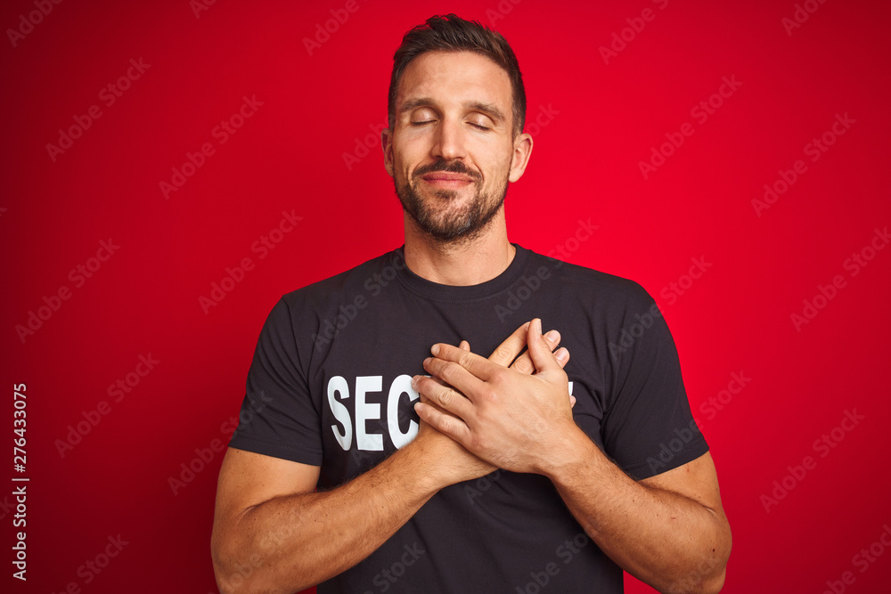 Young safeguard man wearing security uniform over red isolated background smiling with hands on chest with closed eyes and grateful gesture on face. Health concept. Young safeguard man wearing security uniform over red isolated background smiling with hands on chest with closed eyes and grateful gesture on face. Health concept.