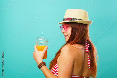 Woman wearing swimsuit and hat drinks fruit juice from a cup