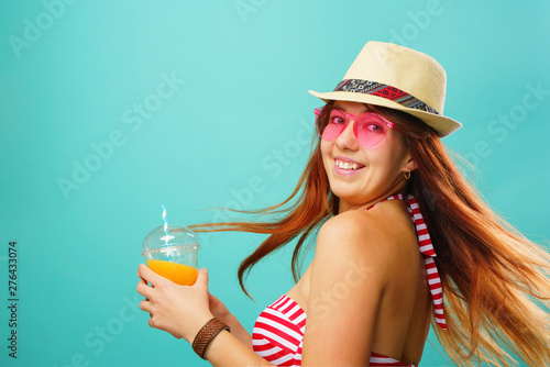 Woman wearing swimsuit and hat drinks fruit juice from a cup