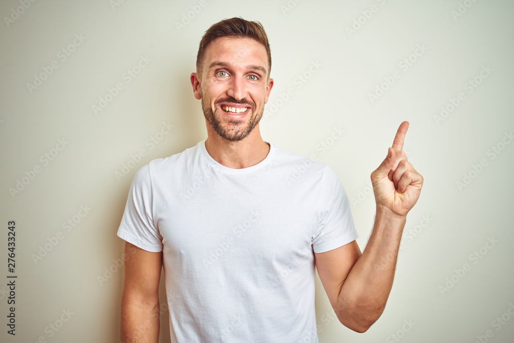 Young handsome man wearing casual white t-shirt over isolated background with a big smile on face, pointing with hand and finger to the side looking at the camera. Young handsome man wearing casual white t-shirt over isolated background with a big smile on face, pointing with hand and finger to the side looking at the camera.