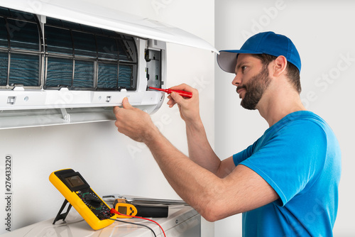 Installation service fix  repair maintenance of an air conditioner indoor unit by cryogenist technican worker with screwdriver  blue shirt baseball cap photo