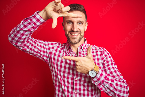 Young handsome man over red isolated background smiling making frame with hands and fingers with happy face. Creativity and photography concept.