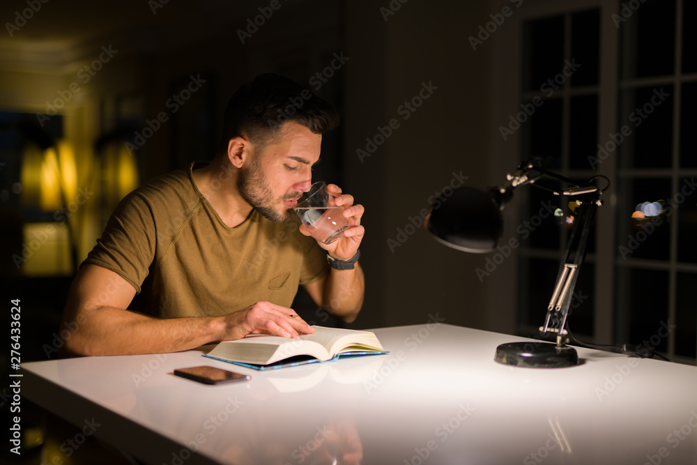Young handsome man studying at home drinking a glass of water Young handsome man studying at home drinking a glass of water
