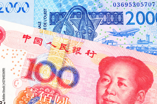 A close up image of a blue, West African franc bank note with a red, one hundred Chinese yuan bank note in macro photo