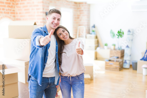 Beautiful young couple moving to a new house doing happy thumbs up gesture with hand. Approving expression looking at the camera with showing success. © Krakenimages.com