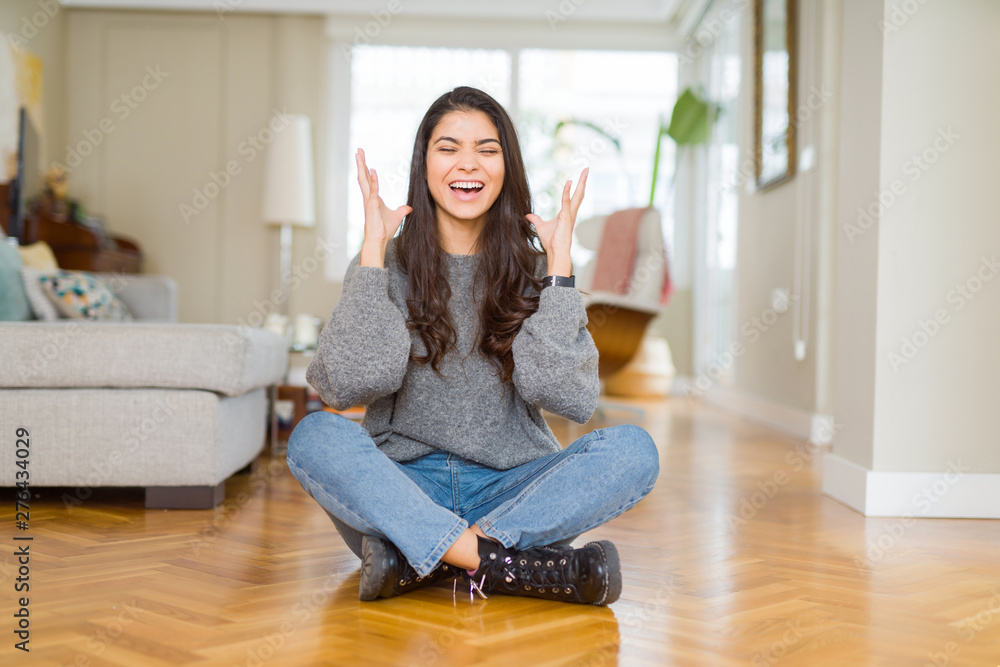 Young beautiful woman sitting on the floor at home celebrating mad and crazy for success with arms raised and closed eyes screaming excited. Winner concept Young beautiful woman sitting on the floor at home celebrating mad and crazy for success with arms raised and closed eyes screaming excited. Winner concept