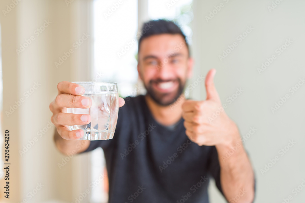 Handsome hispanic man drinking a fresh glass of water happy with big smile doing ok sign, thumb up with fingers, excellent sign Handsome hispanic man drinking a fresh glass of water happy with big smile doing ok sign, thumb up with fingers, excellent sign