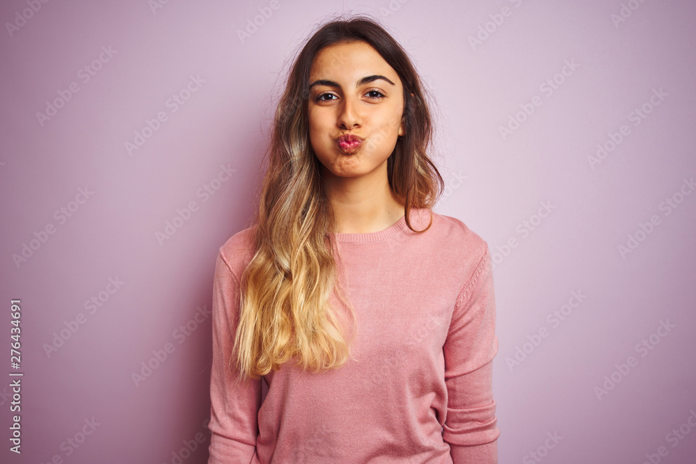 Young beautiful woman wearing a sweater over pink isolated background puffing cheeks with funny face. Mouth inflated with air, crazy expression. Young beautiful woman wearing a sweater over pink isolated background puffing cheeks with funny face. Mouth inflated with air, crazy expression.