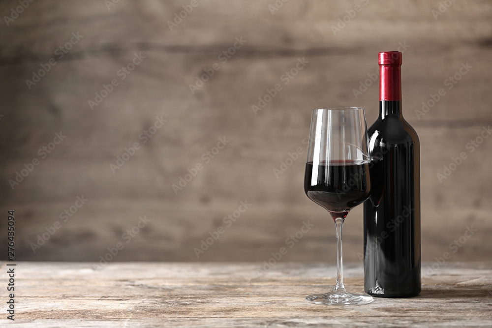 Glass and bottle of red wine on wooden table. Space for text