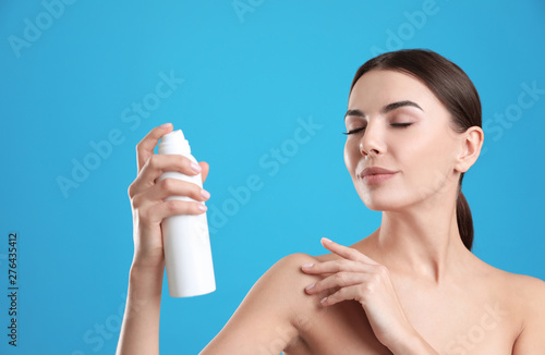 Young woman with bottle of thermal water on color background. Cosmetic product