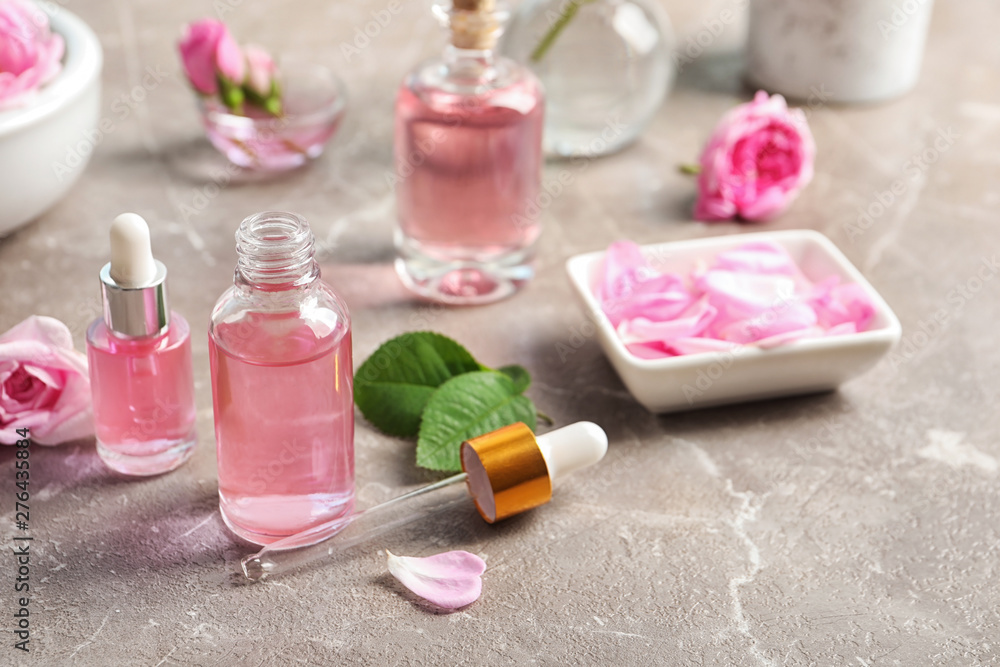 Bottles of rose essential oil, pipette and flowers on table, space for text Bottles of rose essential oil, pipette and flowers on table, space for text