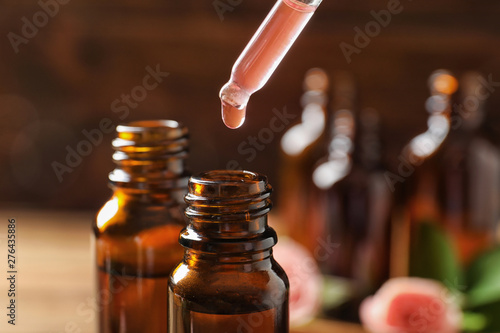 Dripping rose essential oil into bottle against blurred background