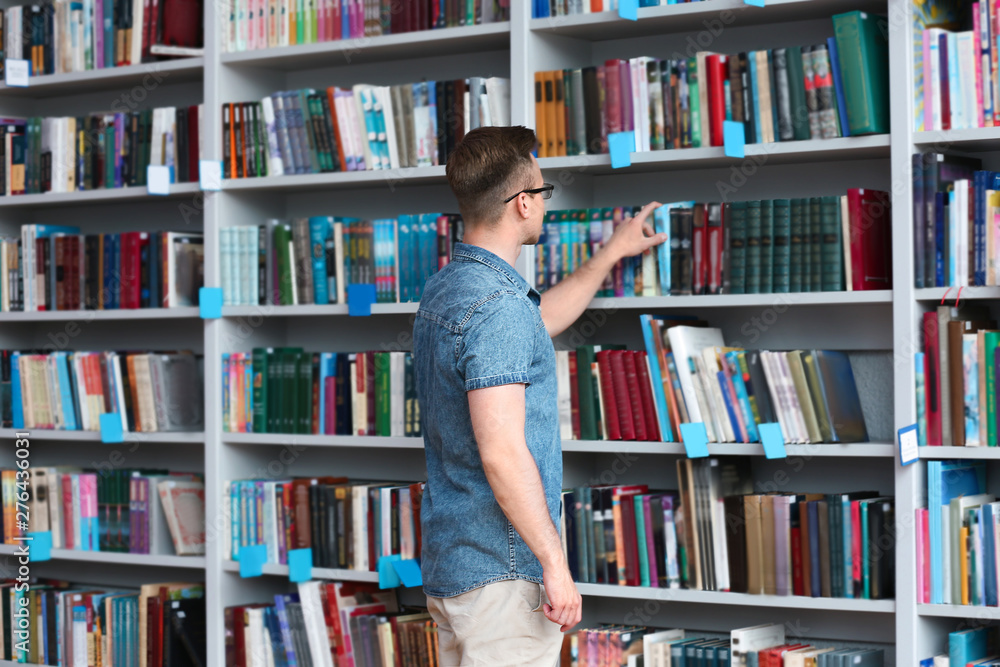 Young man taking book from shelving unit in library Young man taking book from shelving unit in library