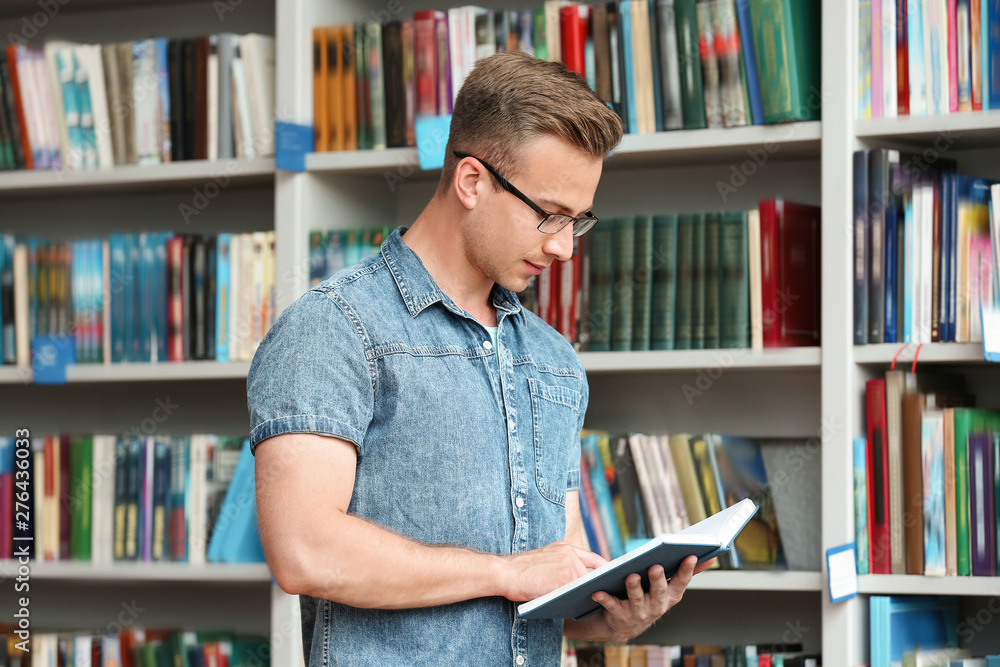 Young man with book near shelving unit in library Young man with book near shelving unit in library
