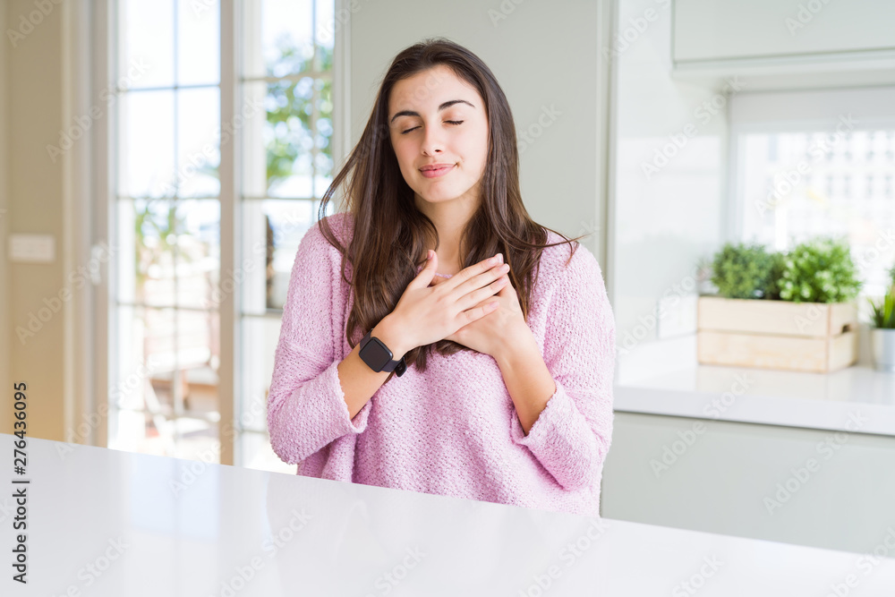 Beautiful young woman wearing pink sweater smiling with hands on chest with closed eyes and grateful gesture on face. Health concept. Beautiful young woman wearing pink sweater smiling with hands on chest with closed eyes and grateful gesture on face. Health concept.