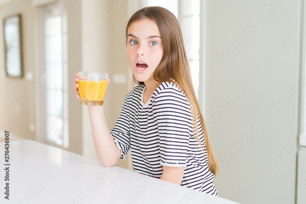 Beautiful young girl kid drinking a glass of fresh orange juice scared in shock with a surprise face, afraid and excited with fear expression Beautiful young girl kid drinking a glass of fresh orange juice scared in shock with a surprise face, afraid and excited with fear expression
