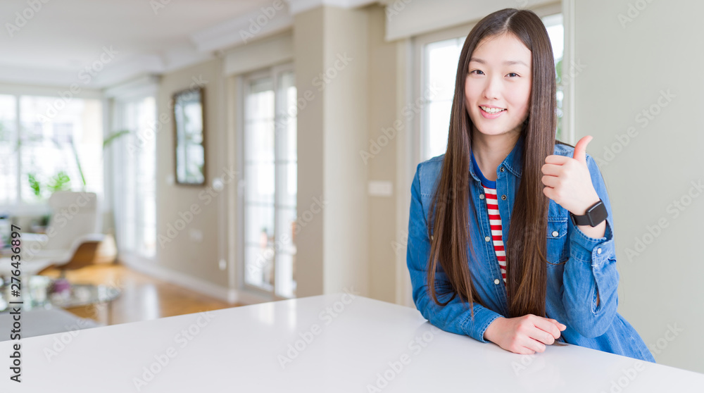 Young beautiful asian woman with long hair wearing denim jacket doing happy thumbs up gesture with hand. Approving expression looking at the camera showing success. Young beautiful asian woman with long hair wearing denim jacket doing happy thumbs up gesture with hand. Approving expression looking at the camera showing success.