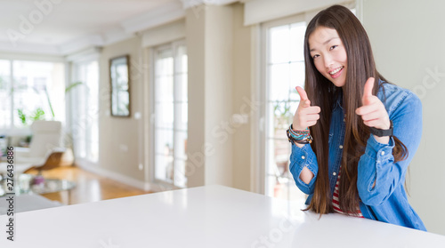 Young beautiful asian woman with long hair wearing denim jacket pointing fingers to camera with happy and funny face. Good energy and vibes.
