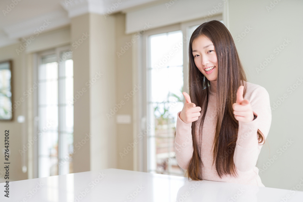 Beautiful Asian woman wearing casual sweater on white table pointing fingers to camera with happy and funny face. Good energy and vibes. Beautiful Asian woman wearing casual sweater on white table pointing fingers to camera with happy and funny face. Good energy and vibes.